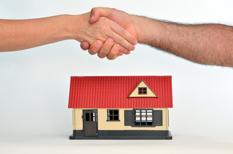 Man and a woman shaking hands over a toy house on white background - copy space.Concept photo of real estate business, home Insurance, house rental, buying, renting, mortgage, selling, finance.